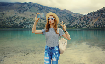 Summer vacation, happy young woman tourist taking selfie with mobile phone wearing straw hat with...
