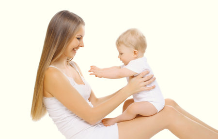 Portrait of happy cheerful smiling mother holding her baby, joyful young mom and little child laughing on white studio backgroundの写真素材