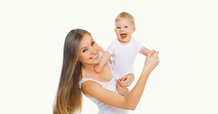 Portrait of happy cheerful smiling mother holding her baby, joyful young mom and little child laughing on white studio backgroundの写真素材