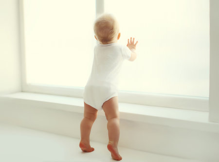 Little baby playing touching window standing in white room at homeの写真素材