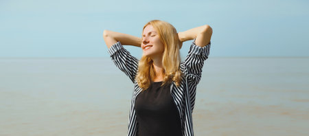 Summer vacation, happy relaxing healthy smiling young woman meditates and enjoying fresh air on the beach on sea coast and blue sky backgroundの写真素材
