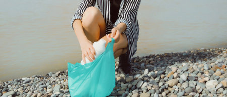 Close-up female volunteer picks up trash on sea beach, eco friendly young woman puts plastic bottles in bag on coast. Recycling, sustainability and climate change, environment or earth dayの写真素材