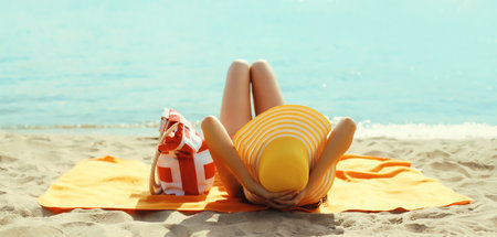 Summer vacation, beautiful happy relaxing young woman with yellow straw tourist hat with bag lying on sand on sea beachの写真素材