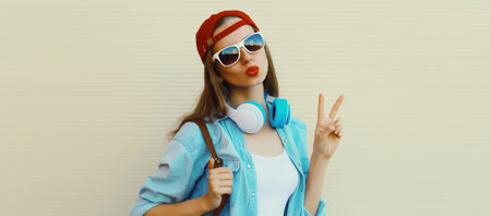 Stylish modern young woman listening to music with headphones, cool girl in baseball cap posing on...