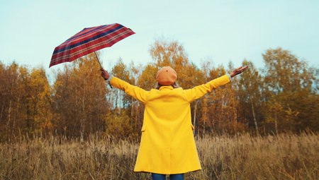 Back view, happy woman in autumn park raising her hands up with umbrella, enjoying warm weather,...