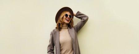 Beautiful stylish happy young woman, fashionable girl smiles in round hat, brown jacket, glasses looking away posing on white studio backgroundの写真素材