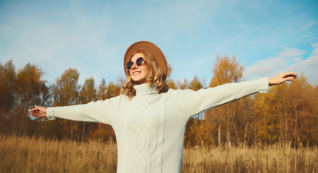 Stylish modern happy young woman having fun and dancing in autumn park, fashionable girl smiling in hat, sweater outdoors, warm fall seasonの写真素材
