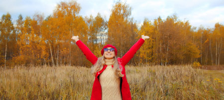 Happy smiling woman in autumn park raising her hands up, stylish joyful girl enjoying warm weather having fun in red jacket outdoors, fall season, nature backgroundの写真素材