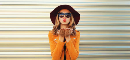 Portrait of beautiful young woman blowing a kiss, stylish girl in hat posing on gray wall backgroundの写真素材