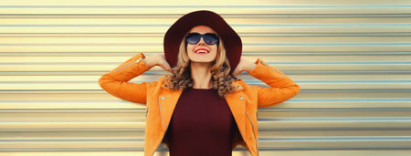 Beautiful smiling young woman wearing orange jacket, round hat on gray backgroundの写真素材