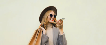 Beautiful happy young woman calling on smartphone with shopping bag, pretty girl smiles wearing hat, glasses standing on white backgroundの写真素材