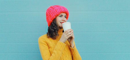 Winter portrait of happy smiling young woman in pink hat, yellow sweater with cup of coffee drink...