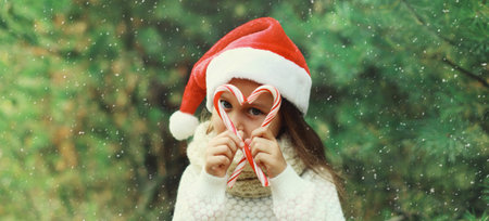 Christmas portrait of happy smiling little girl child in santa red hat with sweet lollipop cane...