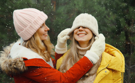 Happy laughing women friends having fun, celebration, joyful girlfriends together on Christmas tree background in winter forest, wearing hat, colorful jacket outdoorsの写真素材