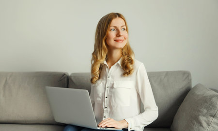 Happy modern young woman working with laptop, freelancer girl looks out the window using computer...