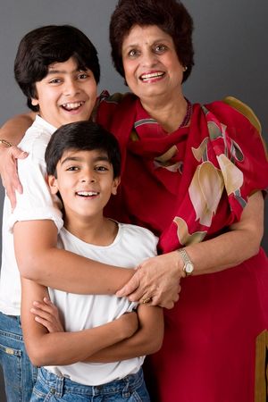 Two children hugging their grandmother against a gray background