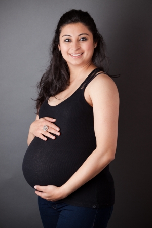 Portrait of a smiling, pregnant East Indian woman holding her bellyの写真素材