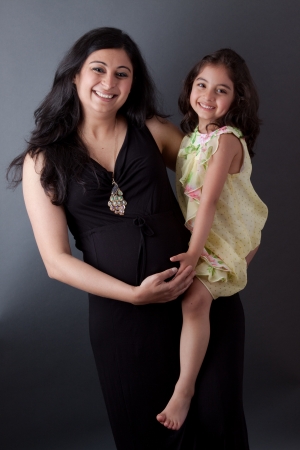 Portrait of a smiling, pregnant East Indian woman sitting with her daughter. The woman is wearing a formal gown.の写真素材