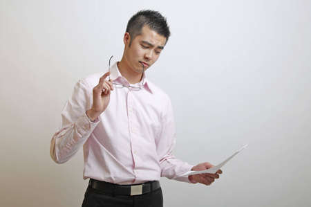 Asian office worker considering how to act on the information he has just readの写真素材