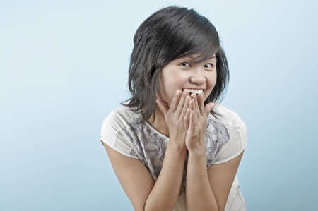 A young Asian woman smiles with her hands by her mouth in a cute pose