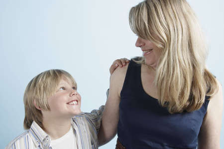 A young boy  looks up to his mother with his hand placed on her shoulderの写真素材