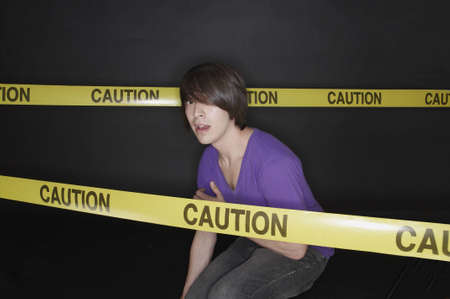 Young man crouching and cordoned off with tapeの写真素材