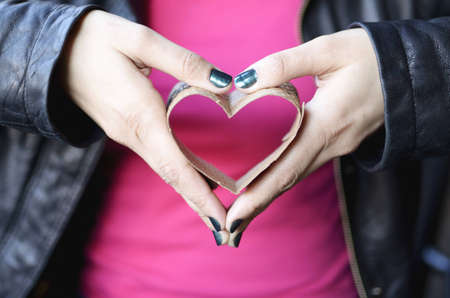 Hands holding a heart formed with a disposable coffee cup insulation sleeveの写真素材