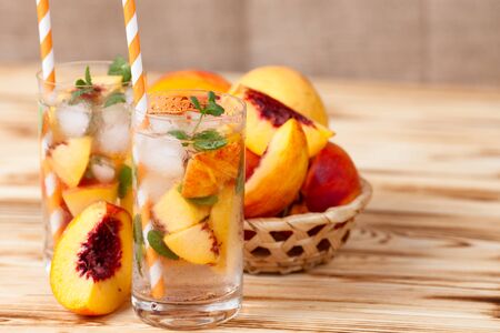 Peach lemonade with ice and mint leaves. Homemade lemonade of ripe nectarine with white and orange ripe. Two glasses of peach tea. Refreshing summer drink. Cocktail on a wooden background.の写真素材