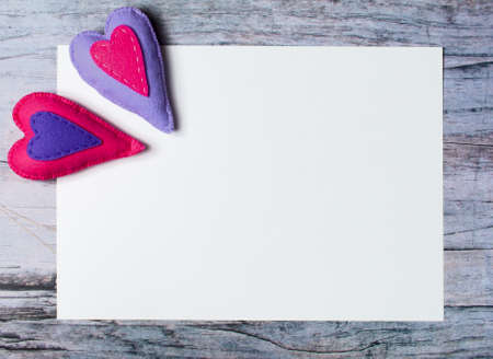 Hand made felt colorful hearts and white paper on wooden background. Concept for congratulation, inviting, wedding banner, flyer. Craft element for Valentine's Day, romantic, greeting, love cardの写真素材