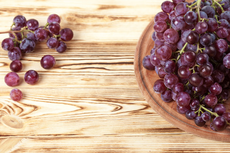Bunches of fresh ripe pink grapes in wicker basket on piece of sackcloth on a wooden textured backdrop. Beautiful background with a branch of green grapes. Top view with copy space. Vintage style.の写真素材