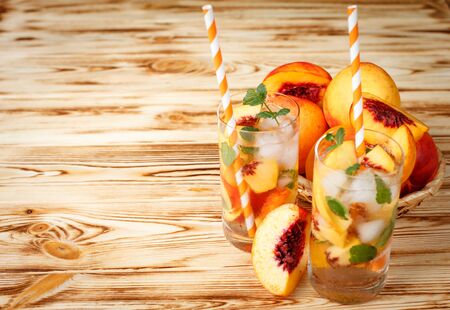 Peach lemonade with ice and mint leaves. Homemade lemonade of ripe nectarine with white and orange ripe. Two glasses of peach tea. Refreshing summer drink. Cocktail on a wooden background.の写真素材