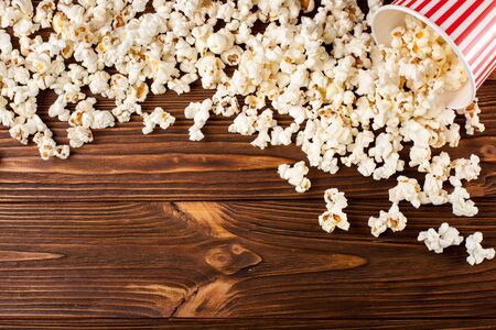 Popcorn horizontal banner. Red stripped paper cup and kernels lying on dark brown wooden background. Copy space. Top view. For cinema card, flyer, invitation.の写真素材