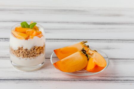 Persimmon creamy trifle in beautiful glasses, fresh ripe fruit slices on white wooden background. Healthy vegetarian food. Delicious dessert. Close up photography. Selective focus. Horizontal banner.の写真素材