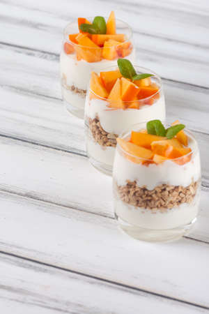 Persimmon creamy trifle in beautiful glasses, fresh ripe fruit slices on white wooden background. Healthy vegetarian food. Delicious dessert. Close up photography. Selective focus. Vertical banner.の写真素材