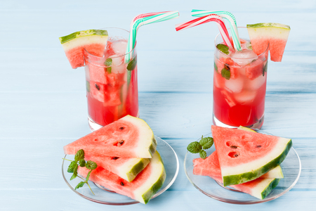 Watermelon lemonade with ice and mint leaves. Homemade lemonade of ripe berry with red and green ripes. Glass of cold watermelon tea. Refreshing summer drink. Cocktail on a wooden background.の写真素材