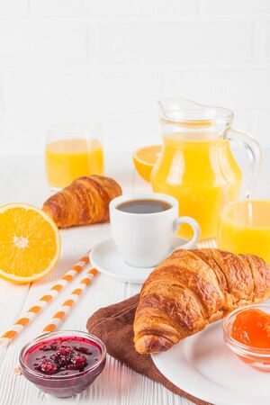 Freshly baked croissant, orange juice, fresh fruits, jam on white wooden background. French breakfast. Fresh pastries for morning. Delicious dessert. Closeup photography. Vertical banner.の写真素材