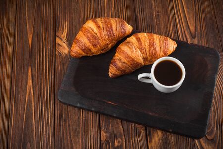 Freshly baked croissant jam, cup of coffee in white cup on brown wooden background. French breakfast. Fresh pastries for breakfast. Modern dark mood style. Delicious dessert. Horizontal banner.の写真素材