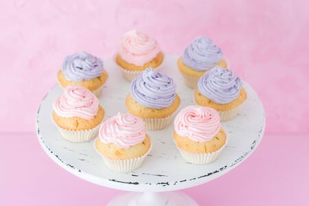 Cupcakes with pink and violet cream on shabby shic stand on pink pastel background. Sweet beautiful decorated cakes. Horizontal banner or greeting card for birthday wedding mothers day.の写真素材