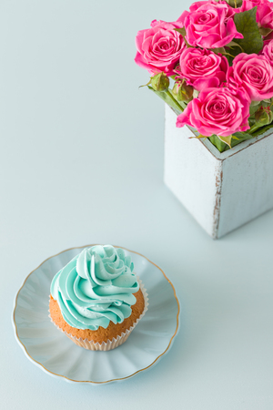 Blue pastel vertical banner with top view of decorated with blue cream cupcake and pink roses in retro shabby chic vase. Beautiful sweets for congratulation poster, greeting card for birthday, weddingの写真素材
