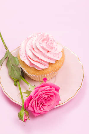 Cupcake with pink cream decoration and roses on pink pastel background - romantic horizontal banner for congratulation, greeting card for birthday, wedding, valentine or women day.の写真素材