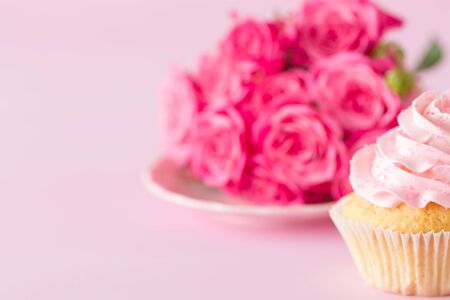Cupcake with pink cream decoration and roses on pink pastel background - romantic horizontal banner for congratulation, greeting card for birthday, wedding, valentine or women day.の写真素材
