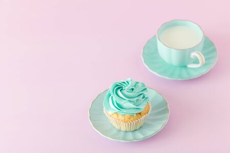 Cupcake with mint cream decoration and cup of milk on pink pastel background with copy space -...