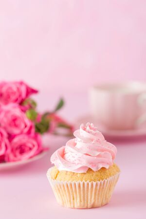 Cupcake with pink cream decoration and roses on pink pastel background - romantic horizontal banner for congratulation, greeting card for birthday, wedding, valentine or women day.の写真素材