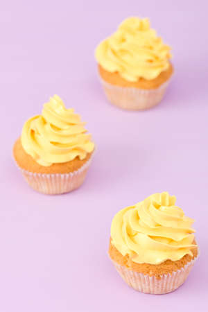 Cupcakes decorated with yellow cream on violet pastel background. Copyspace area. Can be used for greeting, mothers days and valentines card. Minimalism concept.の写真素材