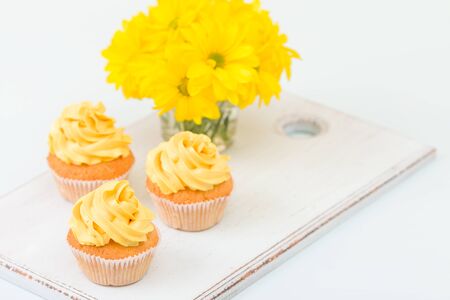 Cupcake with tender yellow cream decoration and bouquet of chrysanthemum in glass vase on yellow pastel background. Can be used for greeting, mothers days and valentines card. Copyspace area.の写真素材