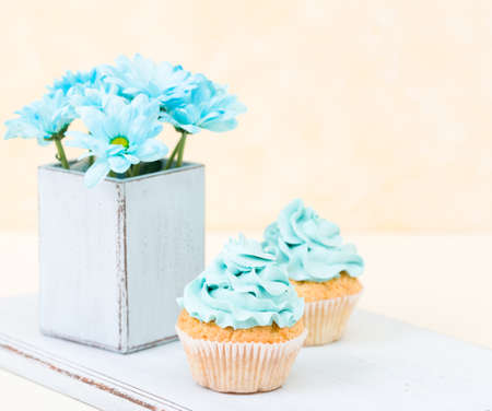 Cupcake with blue cream decoration and blue chrysanthemum in retro shabby chic vase. Yellow pastel banner with copy space for congratulation poster, greeting card for birthday or wedding.の写真素材