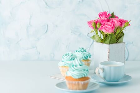 Blue pastel banner with decorated cupcakes, cup of coffe with milk and bouquet of pink roses in retro shabby chic vase. Beautiful congratulation poster, greeting card for birthday or weddingの写真素材