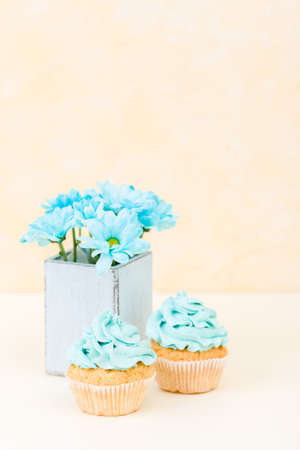 Cupcake with blue cream decoration and blue chrysanthemum in retro shabby chic vase. Yellow pastel vertical banner with copy space for congratulation poster, greeting card for birthday or wedding.の写真素材