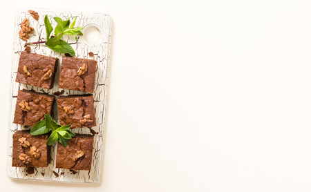 Brownie sweet chocolate dessert with walnuts and meant leaves on retro board with copy space on pastel beige background. Beautiful banner with delicious brown cocoa baked pastry.の写真素材