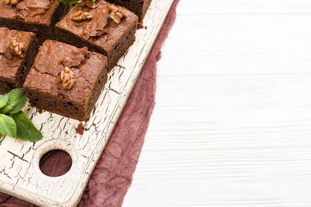 Brownie sweet chocolate dessert with walnuts and meant leaves on retro board with copy space on pastel beige background. Beautiful banner with delicious brown cocoa baked pastry.の写真素材